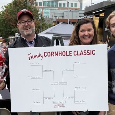 three people hold a Family Cornhole Classic sign.