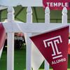 A Temple University pennant hangs from a white picket fence at a fan tailgate.